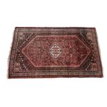 A Qashqai wool rug, on red ground with a central hooked medallion and rosette fillers to the main