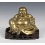 A Chinese brass figure of a seated Buddha, on a carved hardwood stand, 10 x 6in. (25.4 x 15.2cm.),