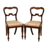Two Victorian rosewood balloon back dining chairs, with carved mid rail over drop in seats, on