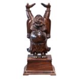 A large Oriental carved hardwood statue of a laughing buddha with his arms raised, standing on a