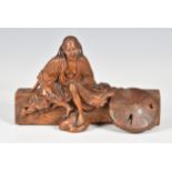 A Japanese carved boxwood okimono of an elderly woman seated upon a log, 19th century, dressed in
