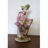 A Sitzendorf porcelain figure of a boy gardener with one foot on his spade, wearing a yellow