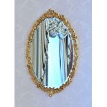 An oval George II style giltwood mirror 20th century, the bevelled plate within a foliate scroll