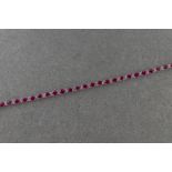 An 18ct white gold ruby and diamond line bracelet, twenty-six oval cut rubies divided by round