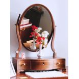 A George III oval mahogany dressing table mirror on a serpentine, three-drawer base with ogee