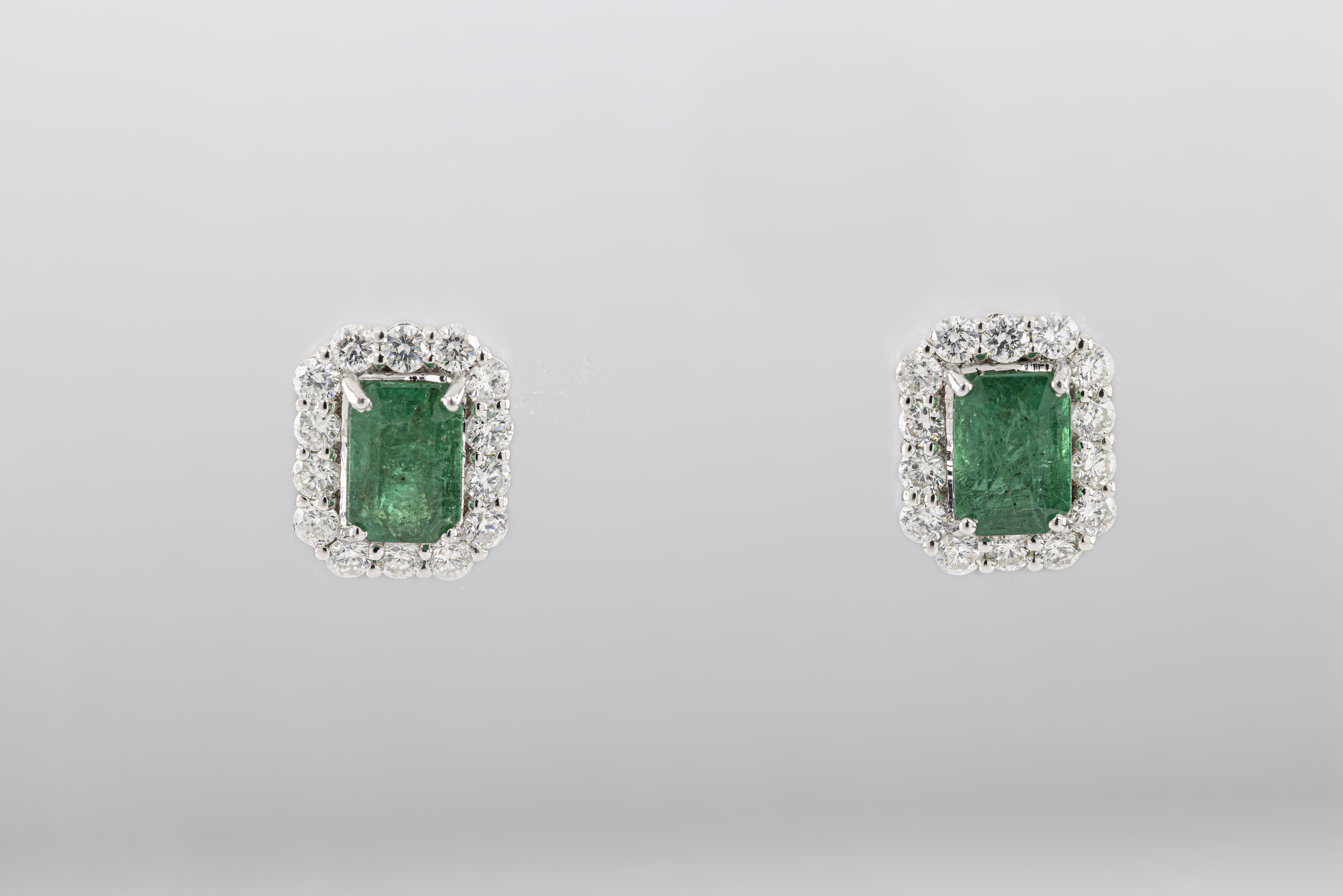 A pair of 18ct white gold emerald and diamond canted rectangular cluster earrings, the emerald-cut