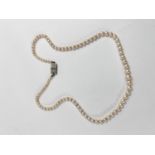 A single strand graduated pearl necklace, with Art Deco style white metal gem set clasp, stamped '