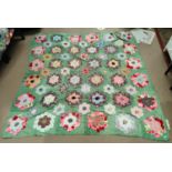 A large patch work quilt (unbacked) with green material with hexagonal pieces in floral shapes,