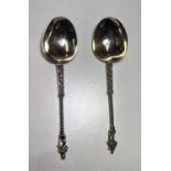 A pair of continental white metal apostle top anointing spoons with monogrammed and gilded bowls.