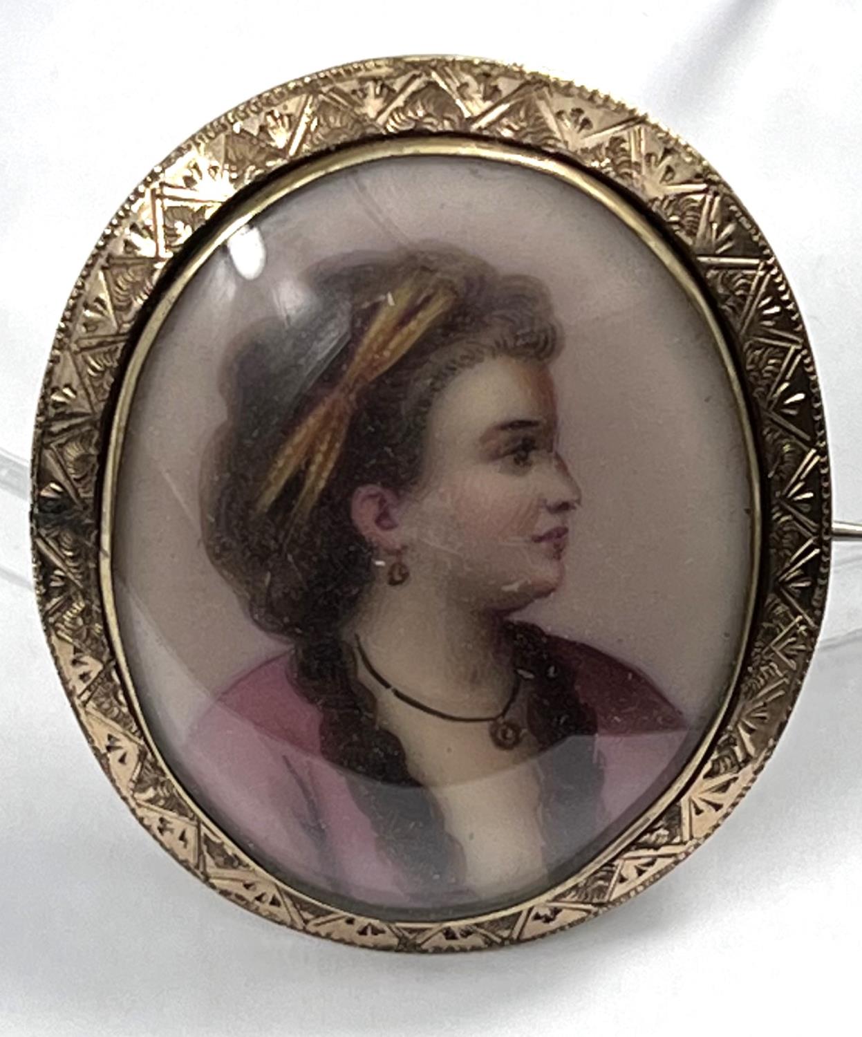 A miniature bust portrait on porcelain brooch of a young lady in 18th century dress in yellow