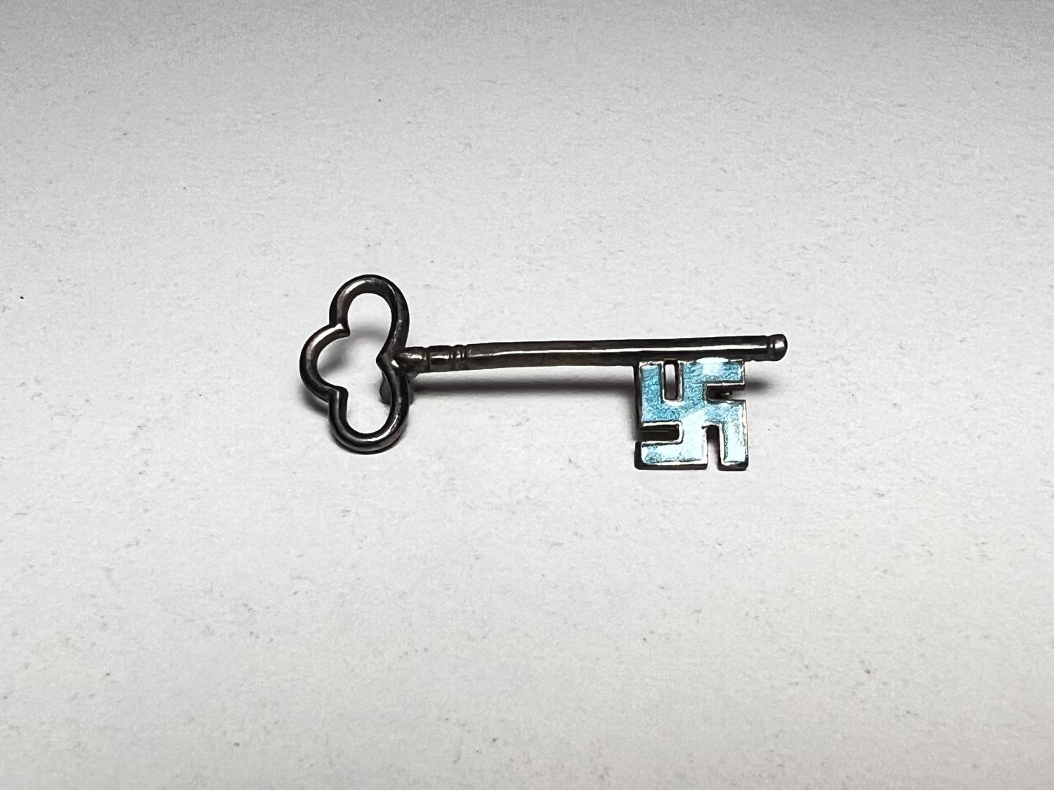 A white metal key shaped brooch with blue enamel Swastika shaped end (pin at back missing)