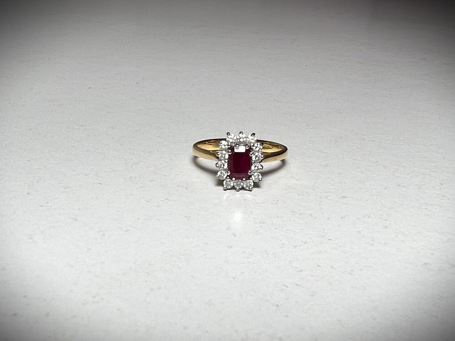 A 18ct hallmarked gold ring set with a central emerald cut ruby surrounded by 14 diamonds.