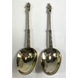 A pair of continental white metal apostle top anointing spoons with monogrammed and gilded bowls.