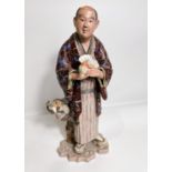 A late 19th/ early 20th century ceramic figure of a man with fan and monkey hanging from his Haori