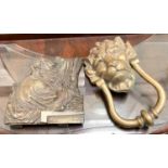 A brass lions head door knocker and a brass depiction of Greek scholar reading