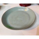A Chinese celadon glazed dish, the under side having incised black characters and seals, diameter