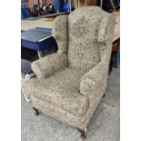 A high wing back armchair upholstered in tapestry style fabric with armorial designs decorating it