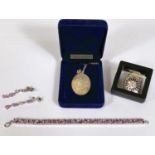 A silver locket in box; a silver QEII commemorative pendant; a white metal bracelet set with pink