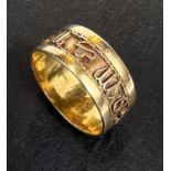 A yellow metal ring with a band of relief hieroglyphs/characters, unmarked, tests as circa 18ct,