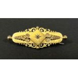 An Edwardian yellow metal bar brooch with scroll and filigree decoration, set small diamond, stamped