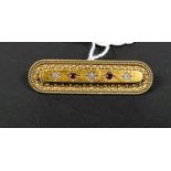 A yellow metal rounded rectangular bar brooch with filigree decoration, set 3 diamonds and 2 rubies,