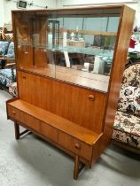 A mid century teak wall unit with sliding glass doors above, cocktail section below and two draws