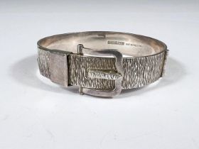 A hallmarked silver bangle in the form of a belt and buckle; an enamel gilt sixpence necklace and