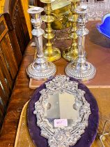 A white metal framed mirror on purple backing, a pair of silver plated candlesticks, two brass and a