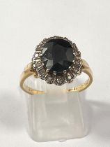 A yellow metal dress ring set faceted oval sapphire surrounded by 14 diamonds, marks rubbed, size