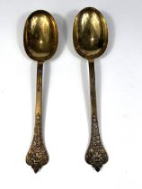 A pair of Edwardian silver/gilt anointing spoons with relief decoration and  facemask trefid