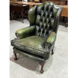 A wing armchair with deep buttoned back upholstered in green leather, on cabriole forelegs