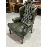 A wing armchair with deep buttoned back upholstered in green leather, on cabriole forelegs