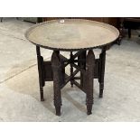 A Benares brass tray top table on carved folding base. 28½' diam