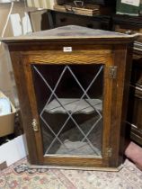 An oak hanging corner cupboard enclosed by a glazed door. 34" high.