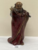 An oriental figure of a sage with a bag of scrolls, wearing a cloak in sang de boeuf glaze. 9½"