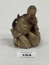 A Chinese carved stone figure of a kneeling man with a basket of fish. 3¼" high. Loss to foot.