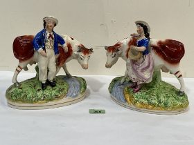 A pair of Staffordshire cow and figure groups. 8¼" high. Losses.