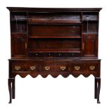 A George III oak dresser, the cavetto cornice above two-shelf boarded rack with spice cupboards with
