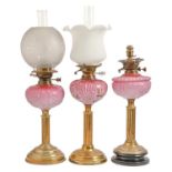 Three Victorian brass oil lamps,  of columnar form, each with scroll moulded pink glass fount (one