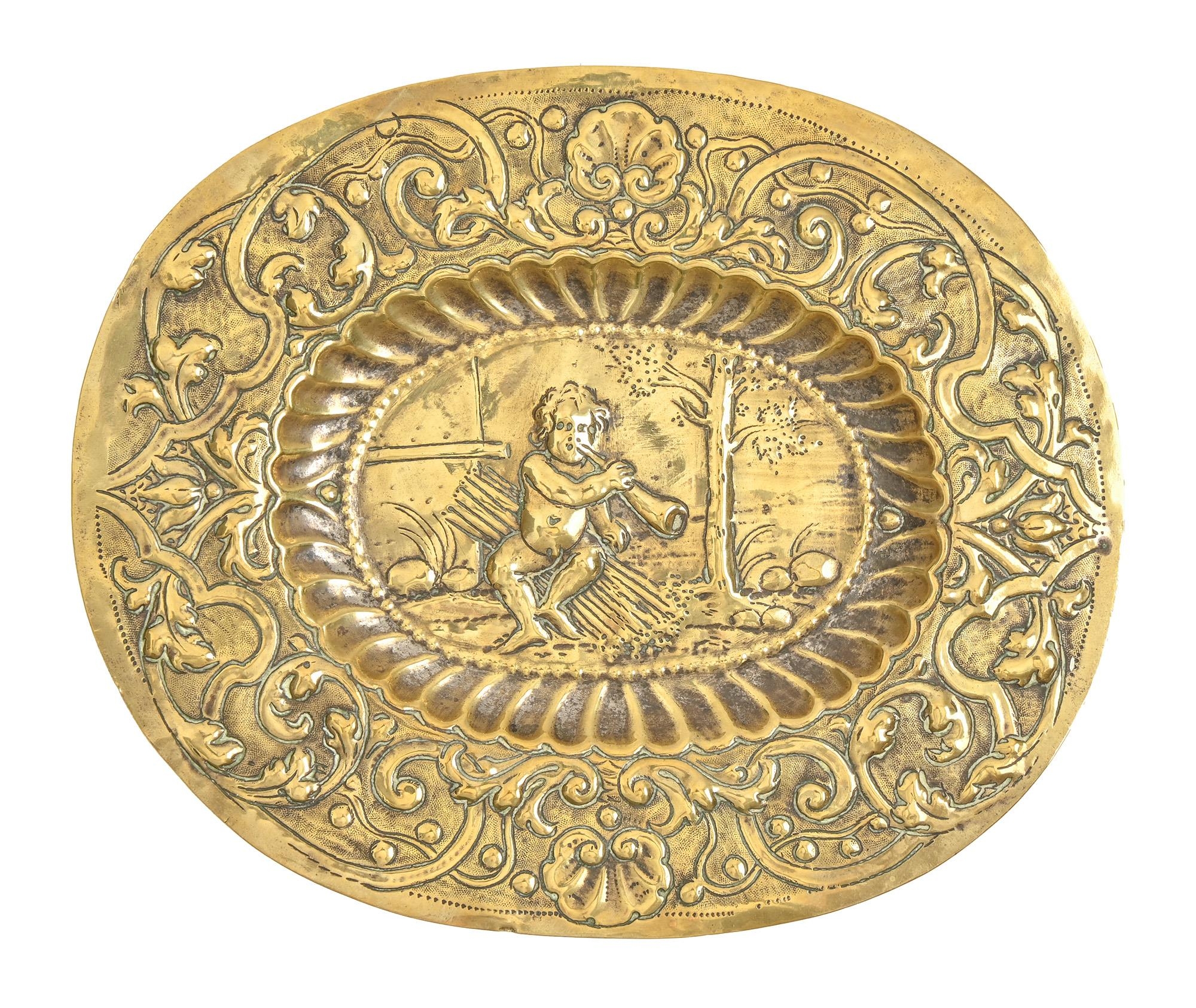 A German brass repousse dish, 17th c, with Putto blowing a horn within fluted cavetto, the border of