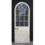 A Victorian arched painted timber door, with glass lights and lower panel, original steel rim lock