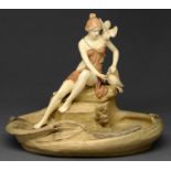 A Royal Dux figural dish, early 20th c, in the form of a maiden with doves on the bank of a lily