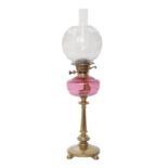 A brass oil lamp, c1900, on round base and four ball feet, moulded cranberry glass fount, brass