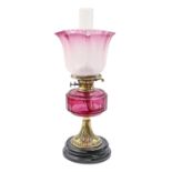 A Victorian stamped brass oil lamp, with faceted cranberry glass fount and brass burner,  on black