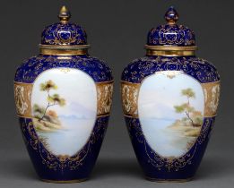 A pair of Noritake jars and covers, c1930, painted with landscapes in oval raised gilt frames