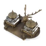 A brass desk stand with central stag's head flanked by two ink wells, enclosed by stacked logs,