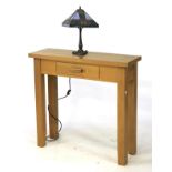 A Morris Furniture contemporary light oak console table with a single drawer and a lamp.