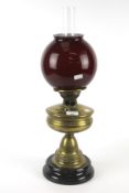 A Victorian brass oil lamp. With red glass globe shade, on a circular ceramic base.