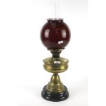 A Victorian brass oil lamp. With red glass globe shade, on a circular ceramic base.