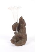 An early 20th century Black Forest carved wooden bear supporting a glass trumpet shaped spill vase.